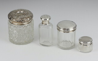 A cylindrical cut glass hair tidy with embossed silver lid (marks rubbed) 8cm, a faceted glass dressing table jar with silver lid Birmingham 1921 and a bottle with silver lid (marks rubbed) 