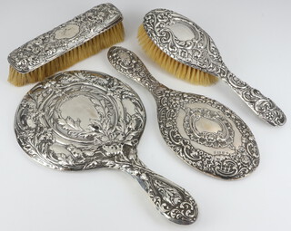 An Edwardian embossed silver backed hand mirror Birmingham 1900 (some holes) together with a silver backed 3 piece dressing table set (some holes) 