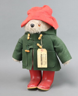 A Paddington Bear with red Dunlop boots, label attached to green duffle coat and red hat 