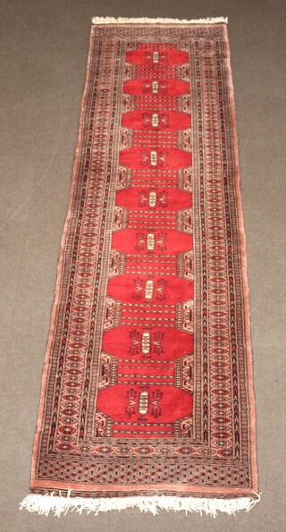 A red and brown ground Bokhara runner with 9 octagons the centre within a multi row border 323cm x 95cm 