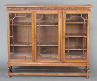 A 1920's carved oak bookcase with carved frieze enclosed by triple astragal glazed panelled door, on spiral turned and block supports with X framed stretcher 124cm h x 146cm w x 31cm d 