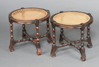 A pair of 1930's circular oak Jacobean style stools with woven cane seats, raised on turned supports with X framed stretchers 41cm h x 47cm diam.  