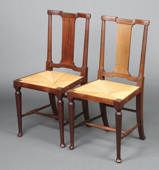 A pair of Edwardian Arts and Crafts mahogany slat back bedroom chairs with woven rush seats raised on club supports 92cm h x 44cm w x 41cm d 