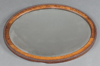 A 1930's oval bevelled plate wall mirror in a decorative oak frame 46cm x 56cm 