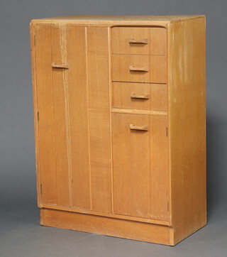 A 1960's G-Plan light oak wardrobe fitted a cupboard flanked by 3 drawers above cupboard, enclosed by a panelled door 121cm h x 88cm w x 45cm d (sun bleached, water and contact marks in places)