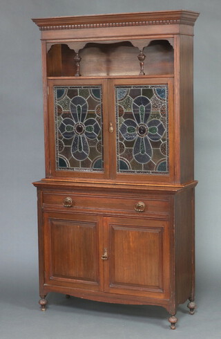 An Art Nouveau oak dresser, the raised back with moulded and dentil cornice above a recess, fitted a cupboard enclosed by lead glazed panelled doors, the base fitted a drawer above cupboard enclosed by pair of panelled doors, raised on turned and reeded bun supports 226cm h x 119cm w x 44cm d  