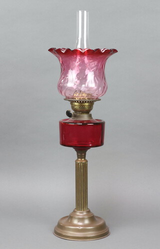 A Victorian cranberry oil lamp reservoir with associated later shade and chimney on a gilt metal reeded column, burner marked T R S 67cm x 14cm 