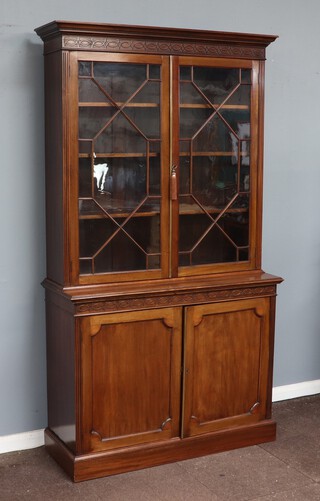 A 19th Century chippendale style cabinet on cabinet with moulded cornice and blind fret work frieze, fitted shelves enclosed by astragal glazed panelled doors with brass bezel, the base with blind fret work frieze above cupboard enclosed by panelled doors, raised on a platform base 218cm h x 119cm w x 43cm d  