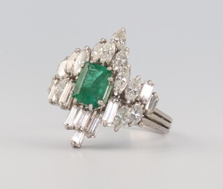 A white metal vintage diamond and emerald cocktail dress ring comprising a baguette cut emerald approx. 1.25ct, 10 baguette cut diamonds each approx. 0.09ct. 12 elliptical cut stones each approx 0.20ct, 7.9 grams, size U 1/2 