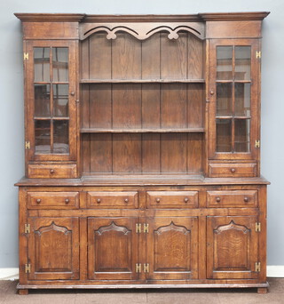 An 18th Century style oak dresser with inverted breakfront, fitted 2 shelves flanked by cupboards enclosed by astragal glazed panelled doors above 2 short drawers, the base fitted 4 short drawers above a cupboard enclosed by 4 panelled doors 101cm h x 184cm w x 53cm d  