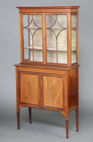 An Edwardian inlaid mahogany display cabinet on cabinet with moulded cornice, the plush interior fitted shelves enclosed by astragal glazed panelled doors, the base enclosed by pair of panelled doors, raised on square tapered supports, spade feet 182cm h x 91cm w x 39cm d 