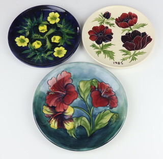 A Moorcroft plate decorated "Hibiscus" on a blue ground, designed by Walter Moorcroft, impressed marks, signature marks and Queen Mary label 26cm, ditto year plate decorated "Anemone" dated 1985, designed by Walter Moorcroft, impressed marks and signature 22cm and ditto limited edition year plate 1990,  no. 174/250 decorated "Buttercup", designed by Sally Tuffin, impressed marks 22.5cm 