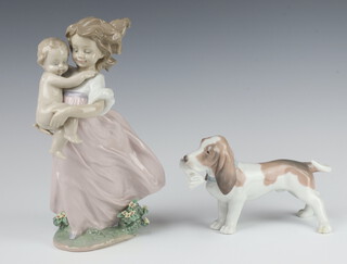 A Lladro figure of a Bassett hound holding a newspaper 11cm,  a Lladro 2000 Event figurine 6681 of a young girl holding a baby 22cm (both boxed) 