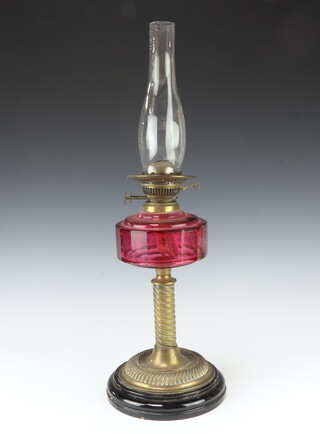 A cranberry glass oil lamp reservoir raised on a metal base with clear glass chimney 64cm h 