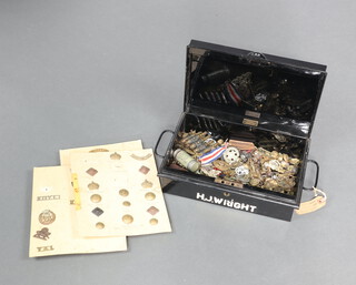 A black metal deed box containing a collection of military cap badges and buttons 