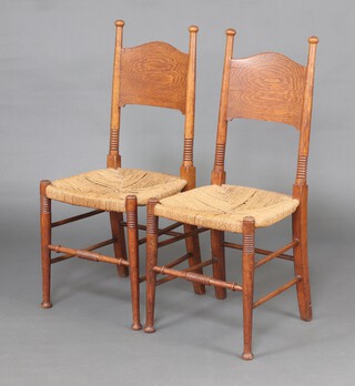 A pair of Arts and Crafts oak bar back chairs with woven rush seats, raised on turned supports 99cm h x 42cm w x 40cm d 