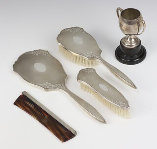 A silver engine turned dressing table set comprising hand mirror, hair brush, clothes brush and comb, Birmingham 1976 together with a silver 2 handled trophy cup, stamped 935 8cm, 67 grams 