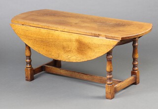 A light oak oval drop flap coffee table, raised on turned and block supports 45cm h x 105cm x 40cm  