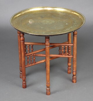 A circular Eastern engraved brass tray raised on a folding beech stand 51cm diam