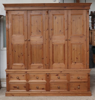 A Victorian style pine triple wardrobe with moulded and dentil cornice, the upper section fitted 2 cupboards enclosed by panelled doors, the base fitted 8 drawers with turned handles 217cm x 205cm w x 73cm d 