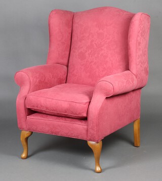 A Victorian style winged armchair upholstered in red material, raised on cabriole supports 109cm h x 81cm w x 71cm d (seat 30cm x 36cm) 