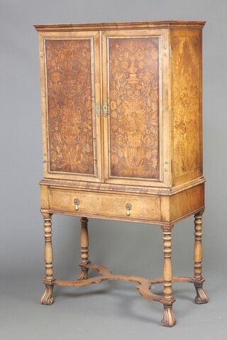 A Queen Anne style inlaid walnut cabinet on stand with moulded cornice, fitted shelves enclosed by floral marquetry panelled doors, the base fitted a drawer, raised on turned supports with X framed stretcher and scrolled supports 162cm h x 85cm w x 45cm d 