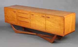 Val Rossi for Beithcraft, a Scottish mid-Century teak sideboard with shaped sides, fitted 3 drawers flanked by a cupboard, cocktail unit and cupboard, raised on shaped supports with an X framed stretcher 74cm h x 205cm w x 46cm d, labelled Beithcraft Ltd. Beith Scotland 