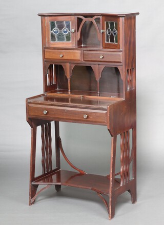 An Edwardian Art Nouveau Liberty style student's bureau, the raised back with niche flanked by 2 cupboards enclosed by lead glazed panelled doors above 2 short drawers, the base with 2 ink well receptacles (ink wells missing) and drawer, fret work to the sides 132cm h x 65cm w x 40cm d 