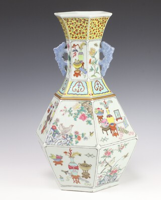 A 19th Century Chinese hexagonal baluster vase decorated with Chinese motifs including table screens, bowls of fruit, koros and vases of flowers alternating with panels of exotic birds amongst flowers, having blue wave handles 42cm 