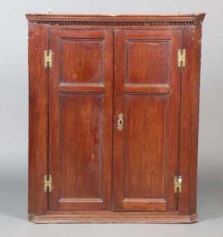 An 18/19th Century hanging oak corner cabinet with moulded and dentil cornice and barrel shaped back, fitted shelves enclosed by panelled doors with H framed hinges 101cm h x 84cm w x 32cm d 