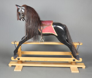 A black painted rocking horse, raised on a rectangular pine base with cruciform supports 130cm h x 160cm w x 48cm d 