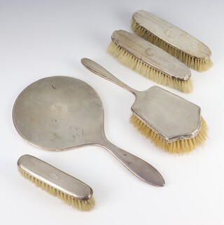 A silver backed engine turned hand mirror Birmingham 1924, 3 similar clothes brushes and a hair brush 