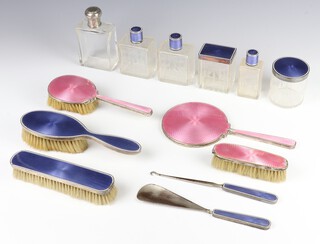 A silver and pink guilloche enamel dressing table set comprising mirror, hairbrush, clothes brush Birmingham 1935 (all bruised) together with a silver and blue guilloche enamel dressing table set with 3 bottles, 2 lidded jars, a hair brush, clothes brush, shoe horn and button hook (1 bottle is bruised, the clothes brush and hair brush and button hook are bruised) and a plated toilet bottle 