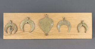 Four Roman gilt bronze Lunula pendants together with a heart shaped ditto, mounted on an oak display stand 