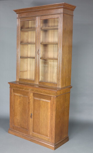 A Victorian oak bookcase on cabinet with moulded cornice, fitted adjustable shelves enclosed by glazed panelled doors, the base enclosed by a panelled door 229cm h x 106cm w x 49cm d 