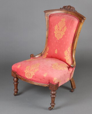 An Edwardian carved walnut nursing chair with scroll crest and turned supports, with red and gilt patterned upholstery 37cm  