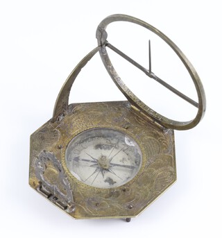 An early 18th Century brass pocket combination sun dial/compass in the manner of L Grafs, contained in an octagonal engraved brass case with a circular silvered compass and blue steel hand under glass, having a folding crescent marked in degrees, with folding pierced brass gnomon the base engraved with latitudes of cities, Elev Pol, Amsterdam 52, Berlin Bremen 53, Hamburg 54, Riga Moscow 57 And Vogl, 6.5cm