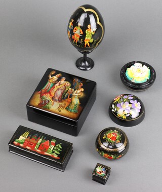 A Russian black lacquered trinket box with hinged lid, decorated buildings, 2cm x 3cm x 3cm, 1 other decorated figures 6cm x 11cm x 11cm, a rectangular box 3cm x 12cm x 5cm, circular jar and cover 4cm x 4cm and 1 other 5cm x 5cm, together with a model egg on stand 10cm x 6cm 