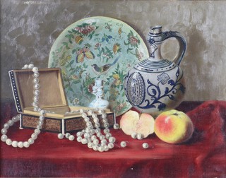 19th Century oil on canvas indistinctly signed, still life study of a Chinese Celadon plate, German ewer, fruits, jewellery box and string of pearls on a red velvet table 38cm x 44cm 