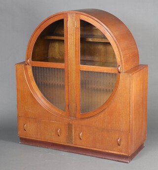 An Art Deco oak circular display cabinet enclosed by a pair of glazed doors, the base fitted 2 drawers 137cm h x 122cm w x 48cm d 