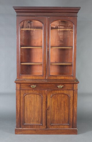 A Victorian mahogany bookcase on cabinet with moulded cornice, fitted adjustable shelves enclosed by arched glazed panelled doors, the base fitted 2 drawers above cupboard enclosed by arch panelled doors, raised on a platform base 212cm h x 111cm w x 48cm d 