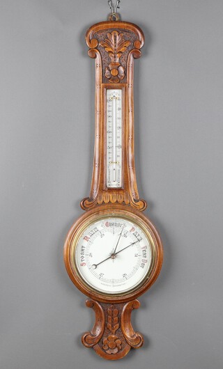 An Edwardian aneroid barometer and thermometer contained in a carved oak wheel case 90cm h x 27cm w