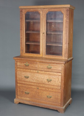 A Victorian bleached oak bookcase on chest, the upper section fitted adjustable shelves enclosed by a glazed panelled doors, the base fitted 2 short and 2 long drawers with brass swan neck drop handles 197cm h x 108cm w x 53cm d  