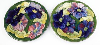 Two Walter Moorcroft plates, decorated the Clematis pattern on a green ground both with impressed marks and Queen Mary label to reverse, 26cm diam each