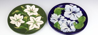 A Moorcroft plate decorated "Bermuda Lily", designed by Walter Moorcroft, signed 26cm diam together with a Moorcroft plate decorated "Blue Hibiscus" designed by Walter Moorcroft, impressed marks, 26.5cm diam