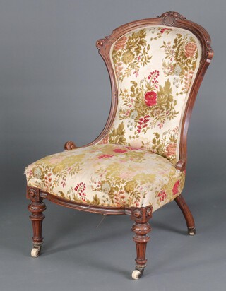 A Victorian carved walnut show frame nursing chair, the seat and back upholstered in floral material, raised on turned and fluted supports with ceramic casters 88cm h x 54cm w x 56cm d (seat 28cm x 30cm) 