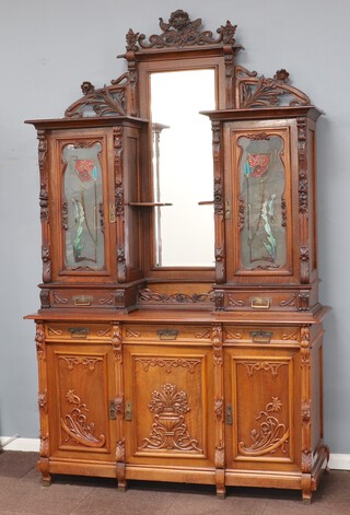 An Art Nouveau large and impressive Continental carved walnut cabinet, the upper section with carved rose decoration and pierced raised back, the centre fitted a rectangular bevelled plate mirror and niche flanked by cabinets fitted shelves enclosed by panelled glass doors etched and painted roses and leaves, the base fitted 3 drawers above triple cupboard enclosed by 3 carved panelled doors 275cm h x 168cm w x 61cm d 