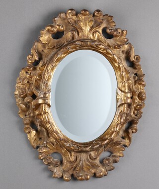 An oval bevelled plate mirror contained in a carved and pierced gilt painted wooden frame 48cm h x 37cm w 