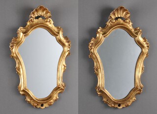 A pair of Rococo style shield shaped plate wall mirrors flanked by shelves, contained in gilt painted wooden frames 41cm x 25cm  