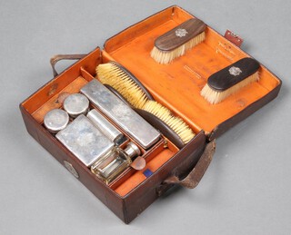 An Edwardian silver mounted travelling toilet set comprising a silver mounted bottle, 4 ditto boxes, travelling shaving brush, 2 clothes brushes with silver monograms, 2 hair brushes with silver monograms, manicure implements, contained in a Mappin & Webb leather case, dated London 1903, maker Charles Henry Dumenil, weighable silver 212 grams 